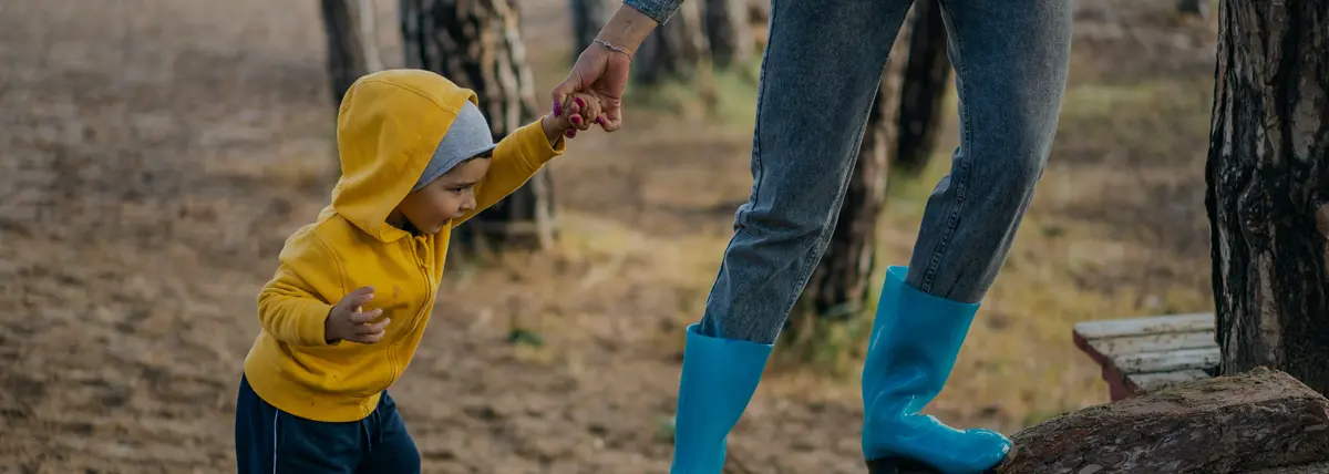 photo of child in yellow hooded sweater walking while holding an adult's hand
