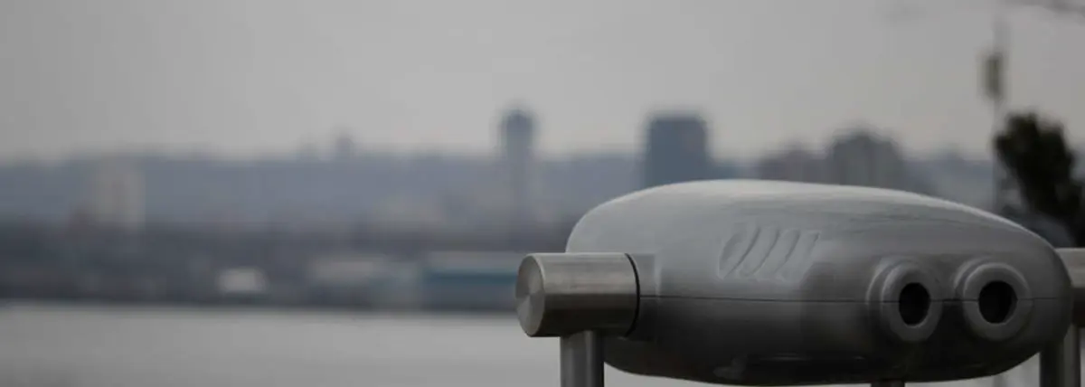 photo of obsevation binoculors in the foreground facing a city in the background that sits behind a large body of water